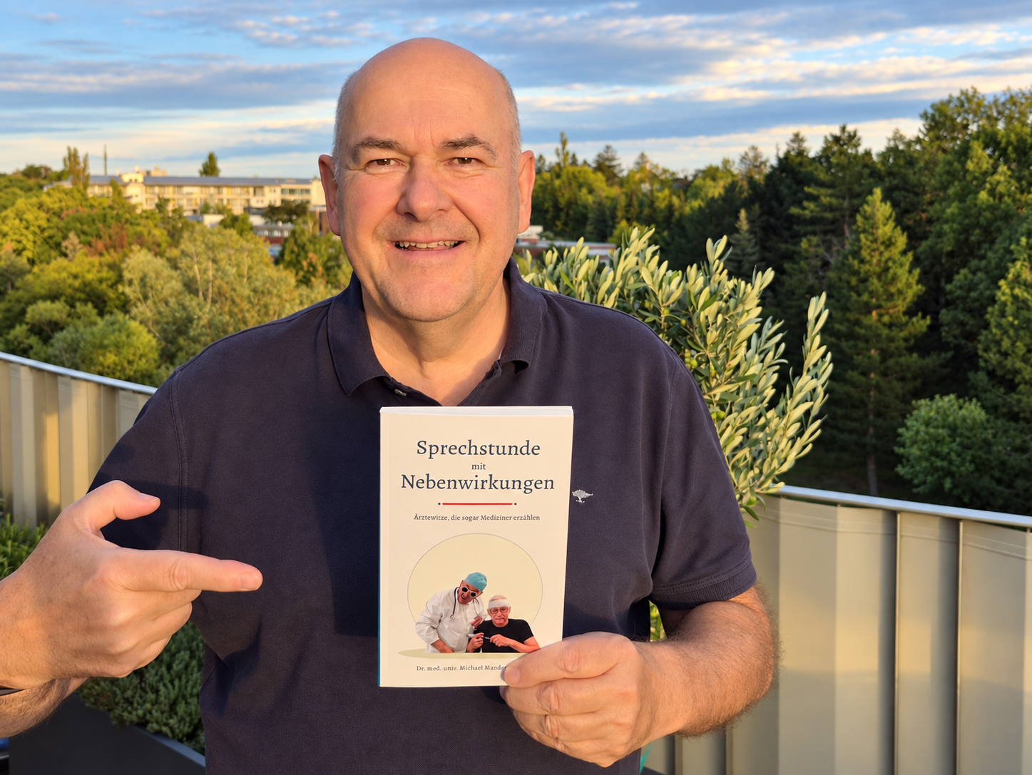 Michael Mandak hält sein Buch „Sprechstunde mit Nebenwirkungen“ in die Kamera und zeigt auf das Cover.